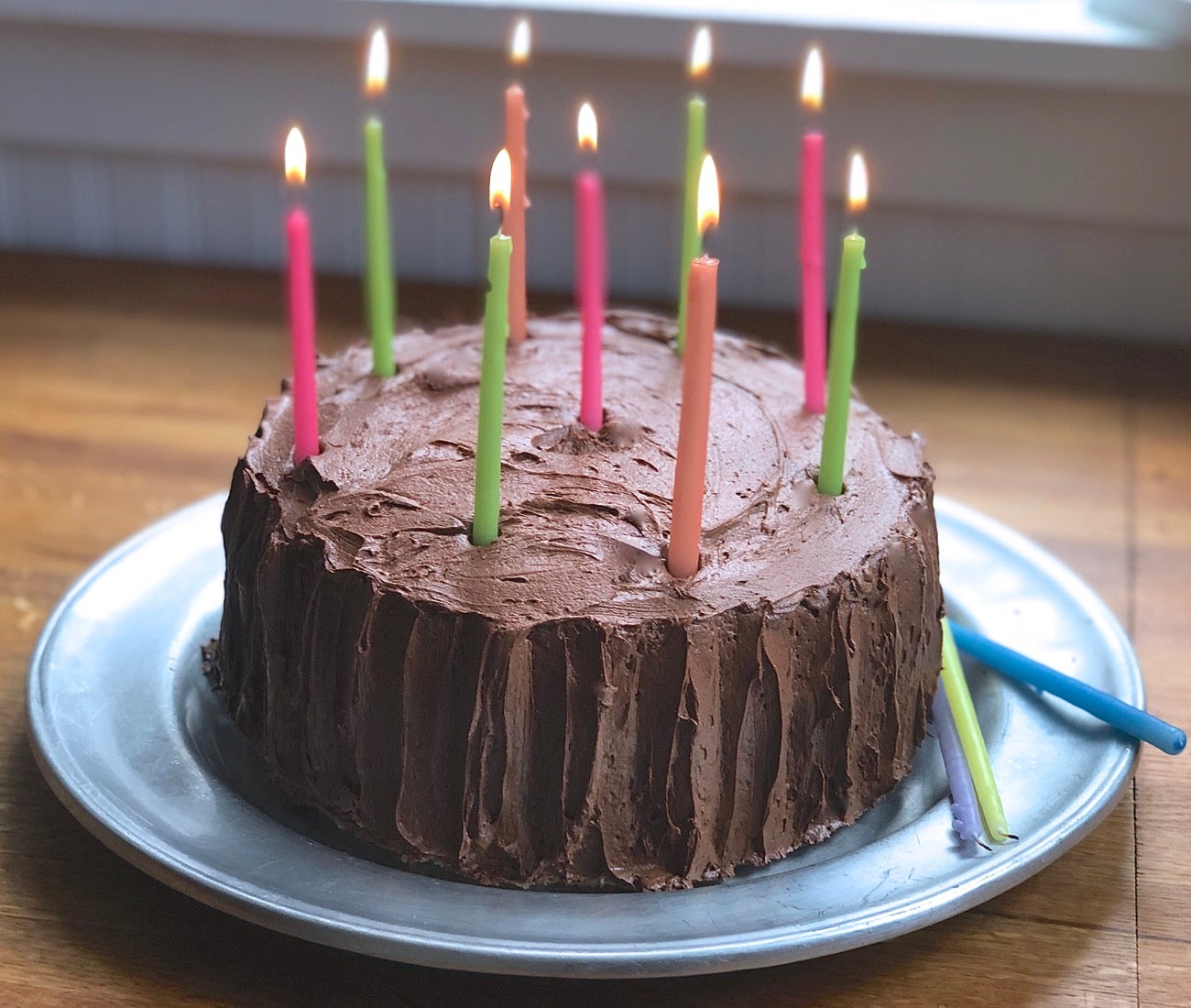 A beautiful yellow layer cake with chocolate frosting and lit candles.